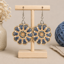 Cargar imagen en el visor de la galería, Blue Blossom embroidered wooden earrings displayed front-facing on a light wood stand.
