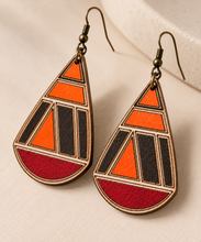 Cargar imagen en el visor de la galería, Close angled view of geometric teardrop wooden earrings showing hand-painted orange, deep red and dark sections, engraved lines, natural wood grain and bronze-tone hooks.