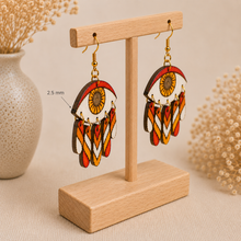 Cargar imagen en el visor de la galería, Radiant Eye hand-painted wooden earrings shown at a steeper angle on the standard light wood stand to clearly display the 2.5 mm wood thickness.