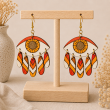 Cargar imagen en el visor de la galería, Radiant Eye hand-painted wooden earrings displayed front-facing on a light wood stand.