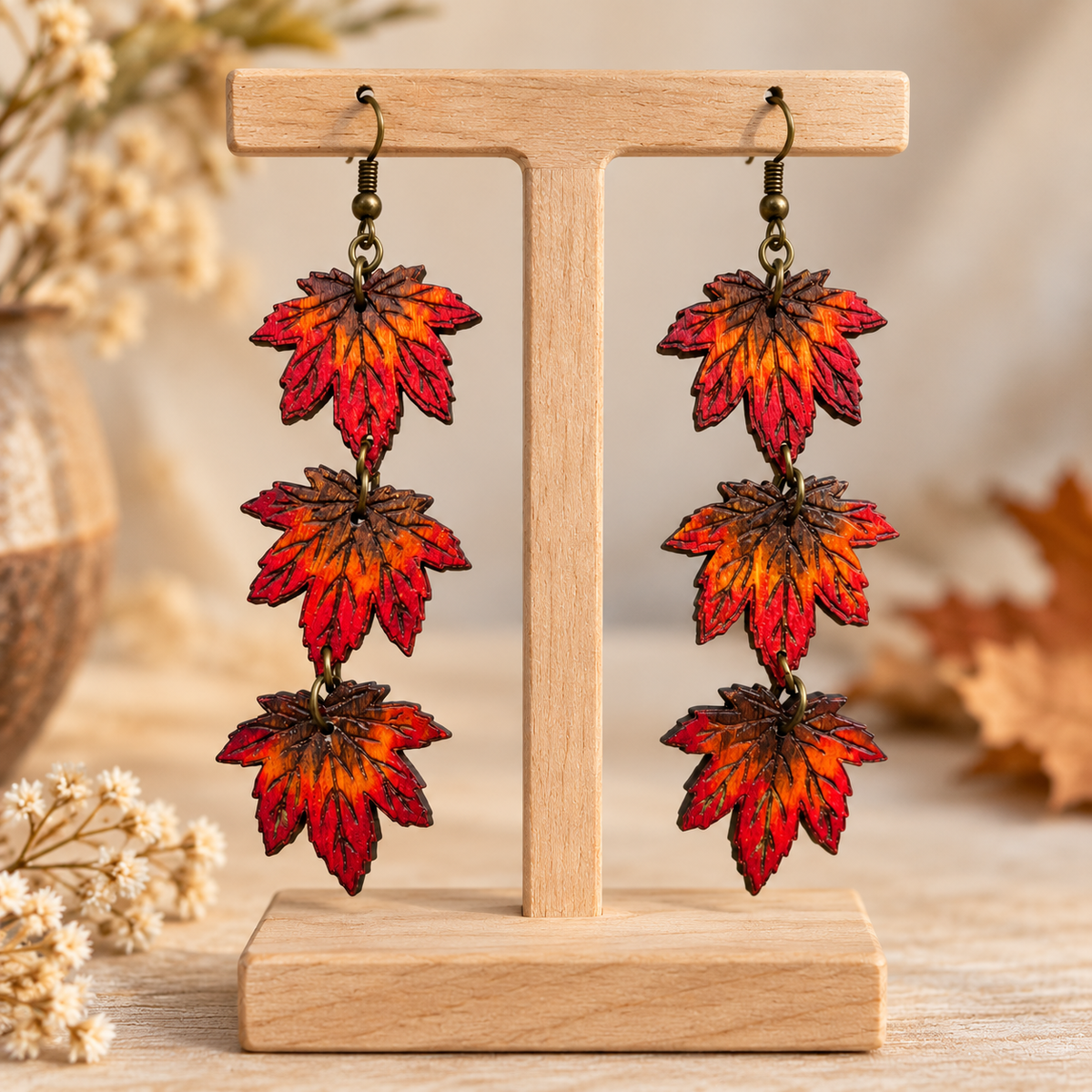 Aretes de madera Autumn Cascade pintados a mano sobre un stand de madera clara, mostrando tres hojas de arce conectadas y ganchos en tono bronce.