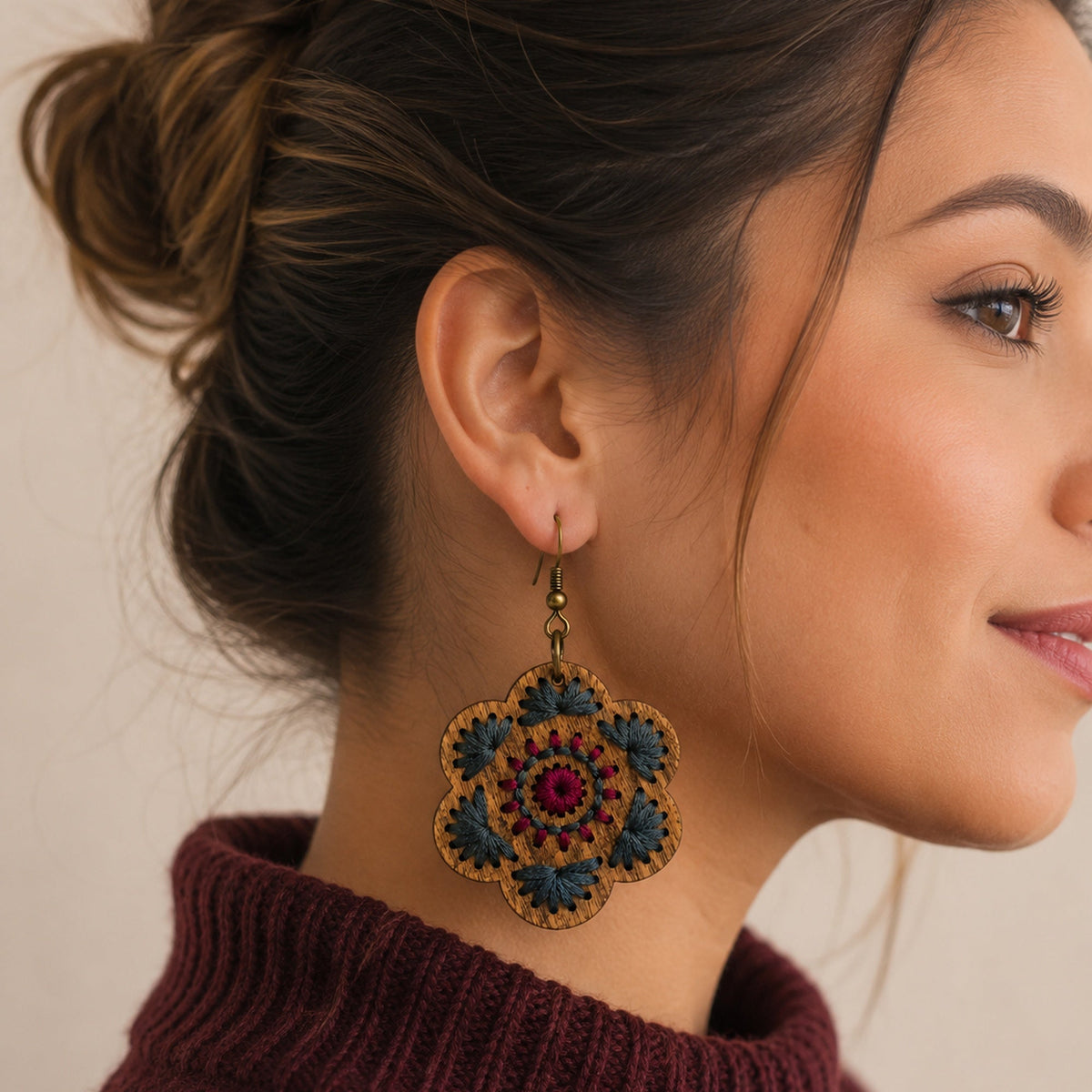 Crimson Roots embroidered wooden earring worn with a burgundy sweater, showing its size and scale.
