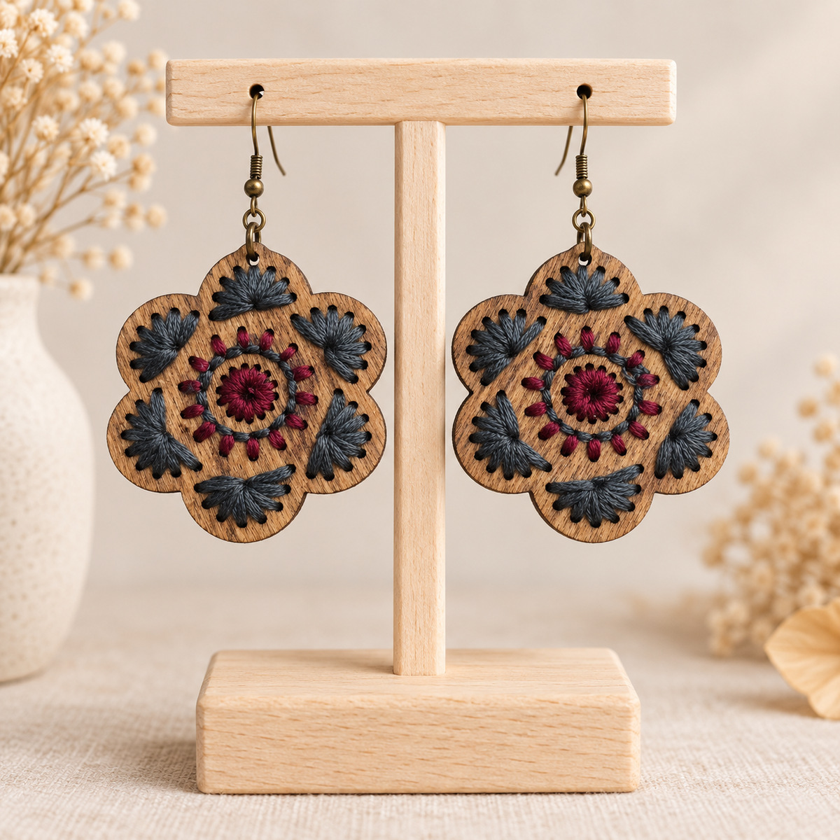 Crimson Roots embroidered wooden earrings displayed front-facing on a light wood stand against a warm cream background.