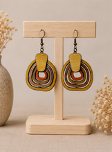 Cargar imagen en el visor de la galería, Earth Echoes hand-painted wooden earrings displayed front-facing on a light wood stand.
