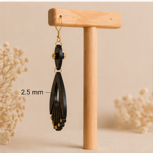 Cargar imagen en el visor de la galería, Side view of Ebony Moon wooden earrings on a light wood stand, showing the 2.5 mm wood thickness.
