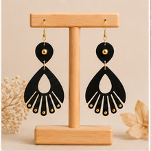 Cargar imagen en el visor de la galería, Ebony Moon wooden earrings shown from the front on a light wood stand, with deep black hand-painted wood and small gold-tone accents.
