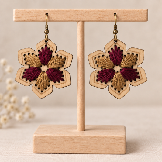 Hand-embroidered floral wooden earrings in burgundy and warm camel on a light wood stand