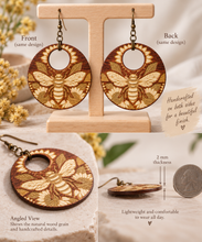 Cargar imagen en el visor de la galería, Front, back and angled views of Sunset Honey Bee wooden earrings showing the same engraved design on both sides and 2 mm thickness
