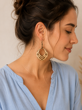 Cargar imagen en el visor de la galería, Model wearing Tribal Spirit engraved wooden earrings with a soft dusty-blue blouse, showing a realistic medium scale and natural wood finish.
